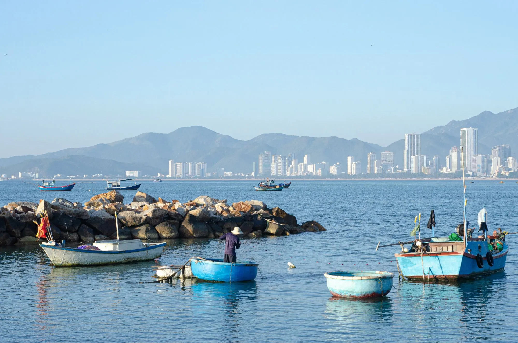 Basket boats and fishing boats on Nha Trang bay, with the city and mountains behind.